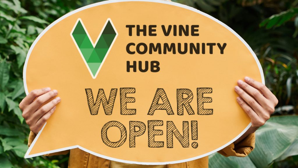 man holding a sign: The Vine Community Hub - We Are Open!